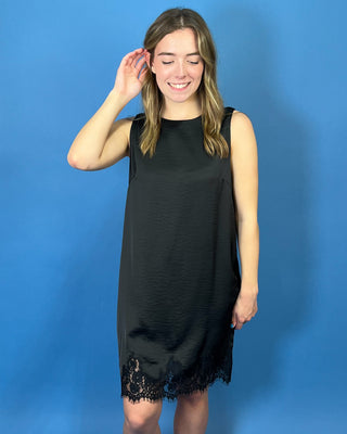 Black sleeveless satin shift dress with a classic round neckline, relaxed silhouette, and delicate lace trim along the hem.