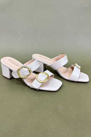 White sandals with gold buckles on a green background
