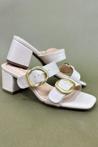 White sandals with gold buckles on a green background