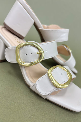 White sandals with gold buckles on a green background