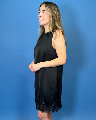 Black sleeveless satin shift dress with a classic round neckline, relaxed silhouette, and delicate lace trim along the hem.