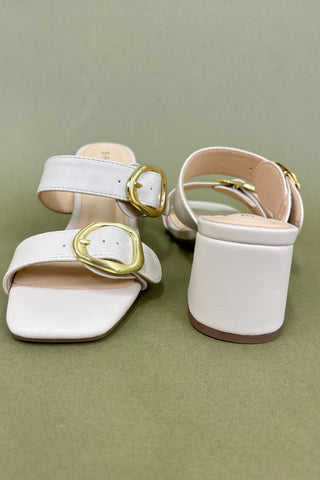 White sandals with gold buckles on a green background