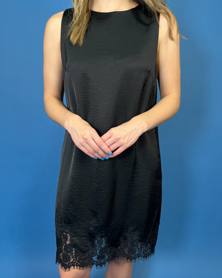 Black sleeveless satin shift dress with a classic round neckline, relaxed silhouette, and delicate lace trim along the hem.