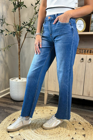 Person wearing blue jeans standing on a woven mat with a plant and wooden cabinet in the background.