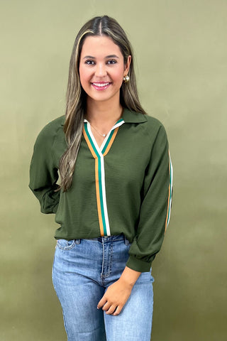 Woman wearing a green long-sleeve top with colorful accents against a beige background
