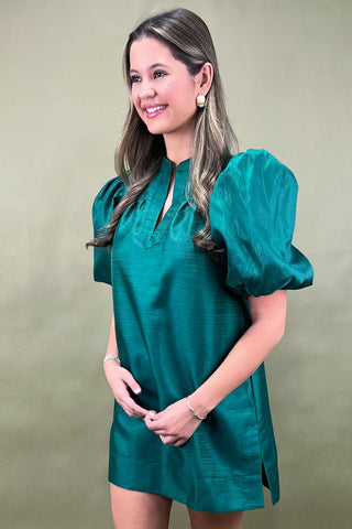 Woman wearing a teal dress with puffed sleeves against a beige background