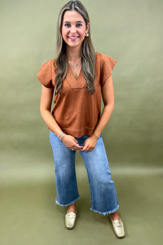 Woman wearing a brown top and blue jeans against a green background