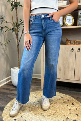 Pair of white and beige sneakers on a denim surface with a plant and jewelry in the background.