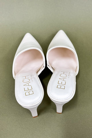 White high-heeled shoes with 'BEACH' branding on a green background