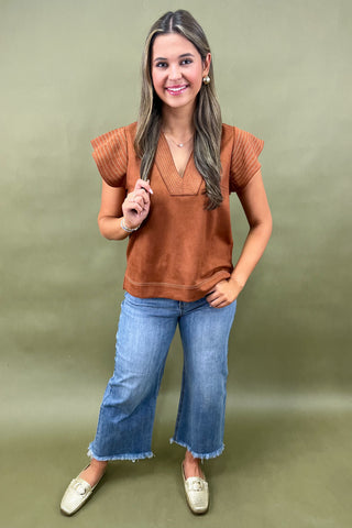 Woman wearing a brown top and blue jeans against a green background