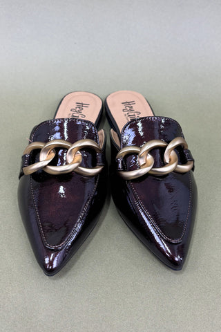 Pair of black patent leather shoes with gold chain details on a light gray background