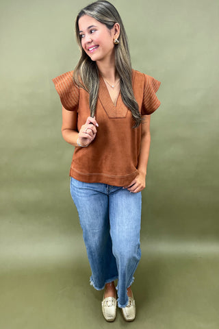 Woman wearing a brown top and blue jeans against a green background