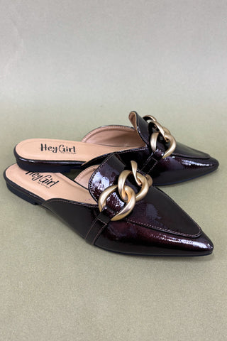 Black patent leather mules with gold chain detail on a light green background