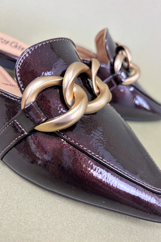 Shiny purple shoes with gold chain detail on a light green background