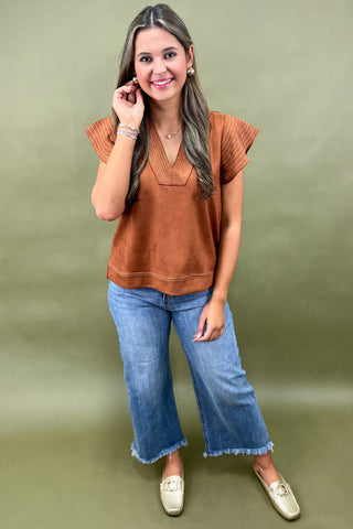 Woman wearing a brown top and blue jeans against a green background