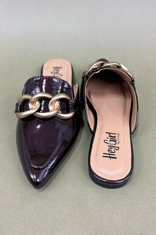 Pair of purple pointed-toe mules with gold chain detail on a light green background