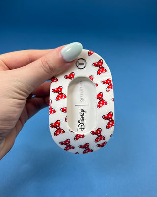 A hand holds a black hair claw clip against a solid blue background. The clip has a white paper label attached to it that reads 'for all hair types' in black text.