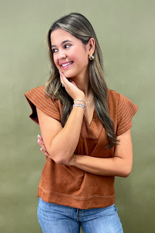Woman wearing a brown top and blue jeans against a green background