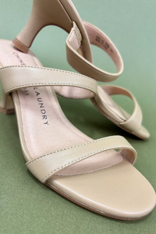 Beige sandals with thin straps on a green background