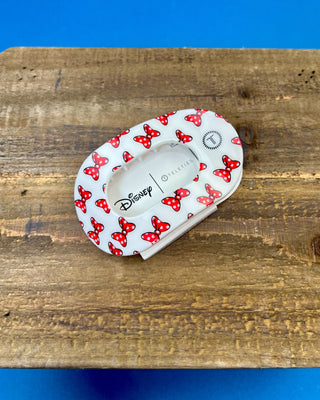 A Disney hair clip with a red and white Minnie Mouse polka dot pattern, resting on a rustic wooden surface with a blue background.
