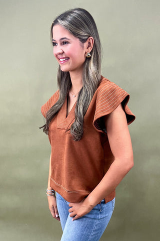 Woman wearing a brown top and blue jeans against a green background
