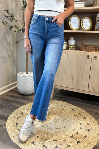 Person wearing blue jeans and white sneakers standing on a round woven rug.