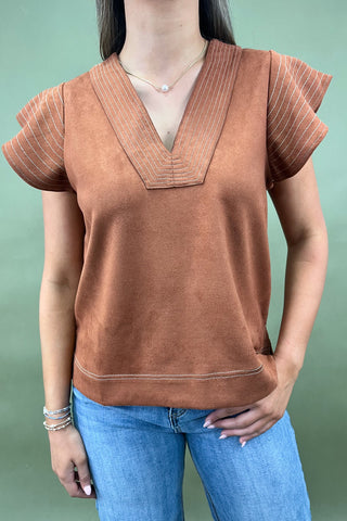 Person wearing a brown top with short sleeves and blue jeans against a green background