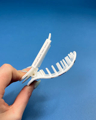 A hand holding a white plastic claw hair clip against a solid blue background.