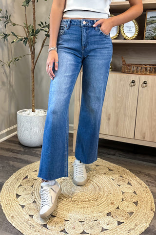 Person wearing blue jeans and white sneakers standing on a round woven rug.