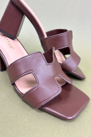Pair of maroon high-heeled sandals on a light green background