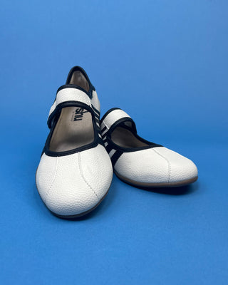 A pair of white Mary Jane-style shoes with black trim and straps, displayed on a solid blue background.