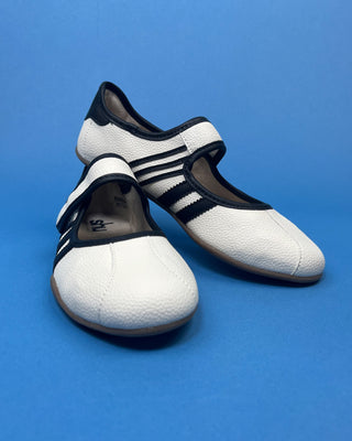 A pair of white pebbled leather Mary Jane shoes with black trim and three stripes, displayed on a solid blue background.