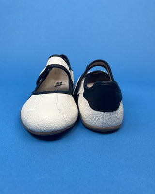A pair of women's slip-on shoes with a white pebbled leather upper and a black heel tab, photographed against a solid blue background.