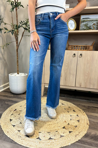 Person wearing blue jeans and white sneakers standing on a round woven rug.