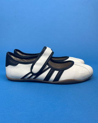 A pair of white pebbled leather Mary Jane shoes with black trim and three stripes, displayed on a solid blue background.