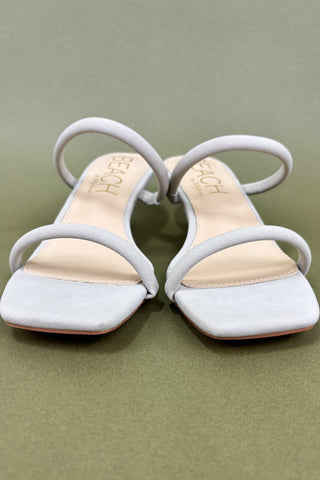 Pair of beige sandals with white soles on a green background