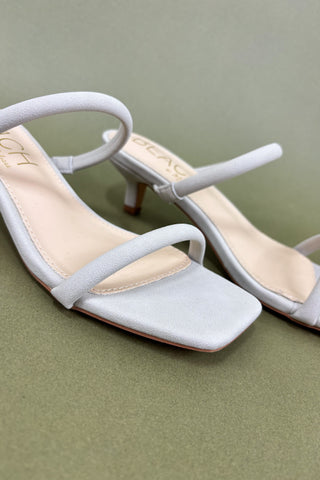 White high-heeled sandals with thin straps on a green background