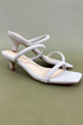 White high-heeled sandals on a green background