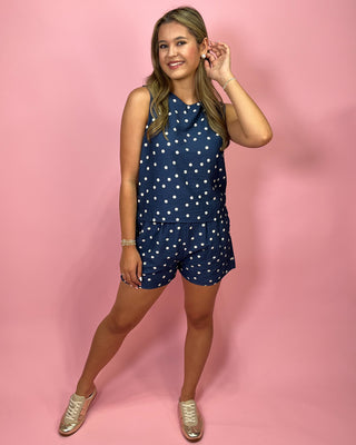 Woman wearing a navy blue romper with white polka dots on a pink background