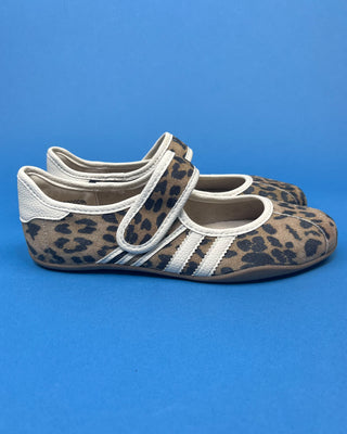 A pair of Mary Jane shoes with a brown and black leopard print pattern and white stripes, displayed on a solid blue background.