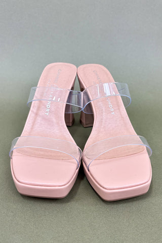 Pink sandals with clear straps on a green background