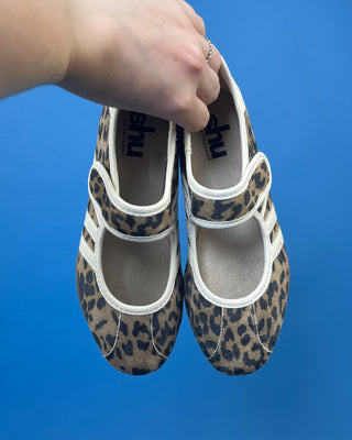 A pair of Mary Jane shoes with a brown and black leopard print pattern and white stripes, displayed on a solid blue background.