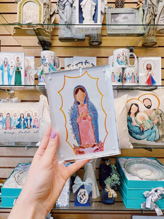 A hand holding a framed print of a religious figure, with other framed artworks displayed in the background.