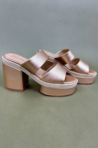 Pair of rose gold sandals with a block heel on a gray background