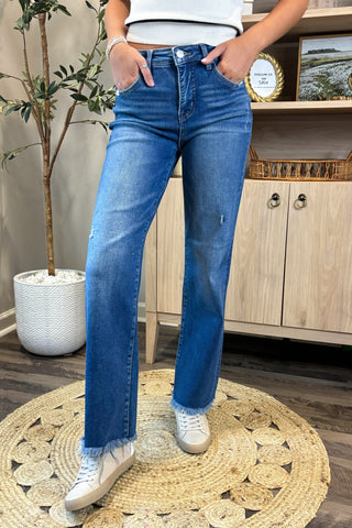 Person wearing blue jeans and white sneakers standing on a round woven rug.