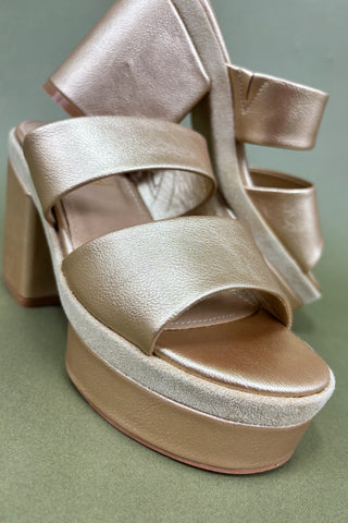Gold platform sandal with a bow on a green background