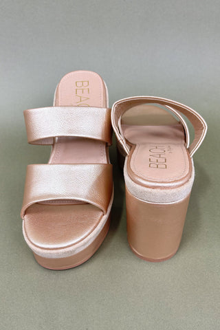 Rose gold platform sandals on a gray background