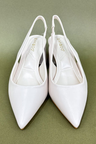 Pair of white pointed-toe slingback shoes on a green background