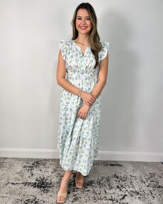 Model wearing a white floral tiered midi dress with flutter sleeves and a smocked waist, styled with nude block-heel sandals.