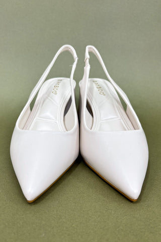 Pair of white pointed-toe slingback shoes on a green background